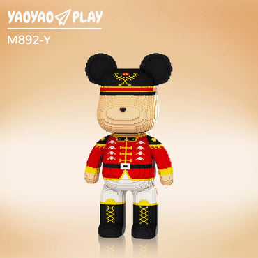 A red-uniformed ​​Brick Bear toy​​ with gold buttons, black cap, and "M892-Y" label on a gradient peach backdrop.